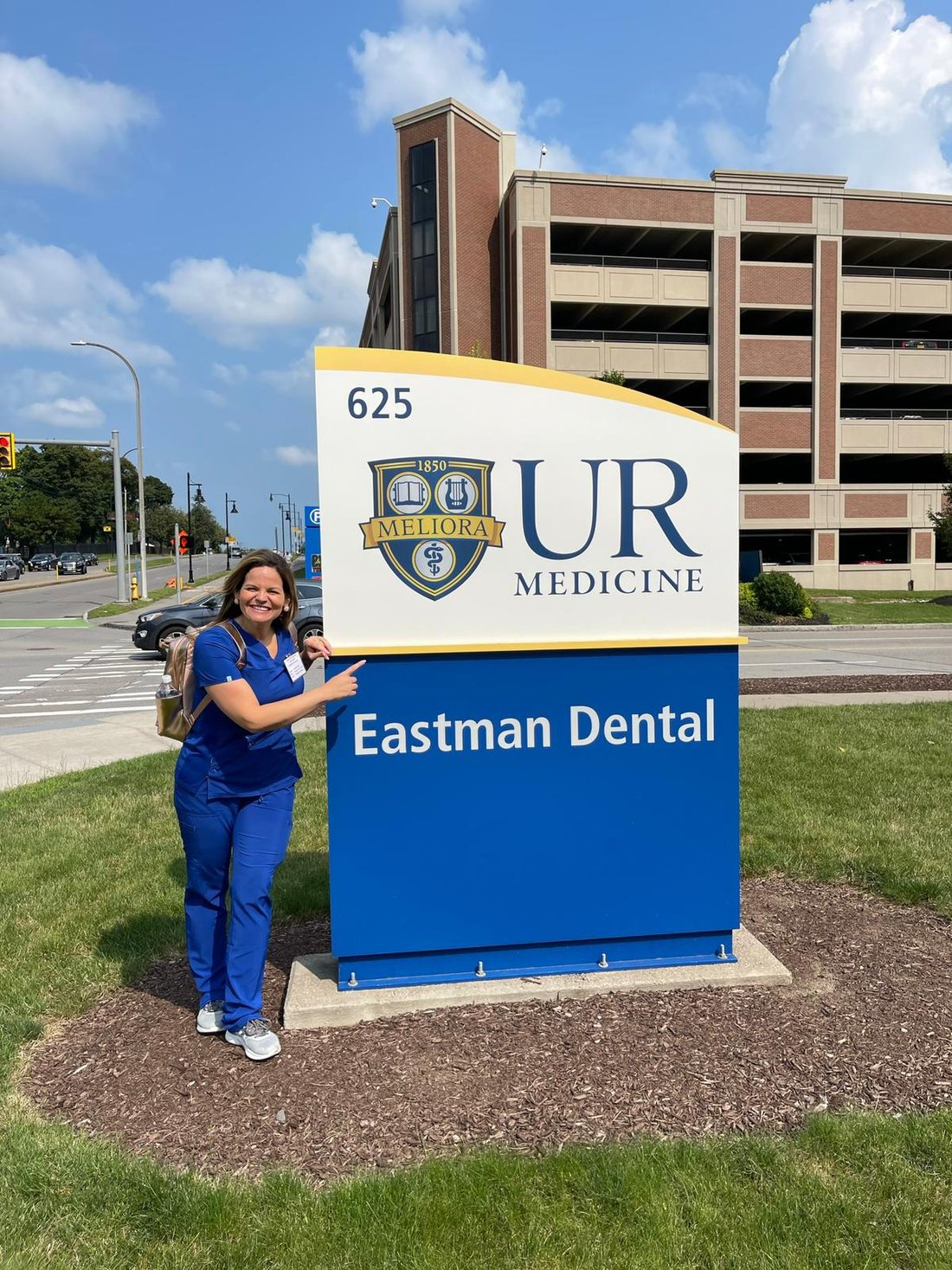 Dr. Raquel de Mello Gomes by the University of Rochester Eastman Dental sign in Rochester, NY